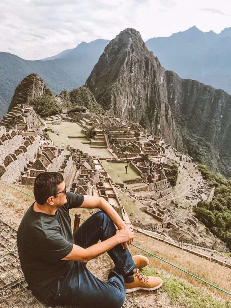 Visitante sentado a olhar para a cidadela de Machu Picchu, com a montanha atrás