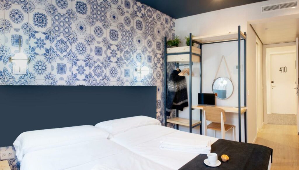 Quarto no hostel Rodamon Lisboa, com duas camas de solteiro juntas a formar uma cama de casal, um toucador com espelho e um armário aberto.