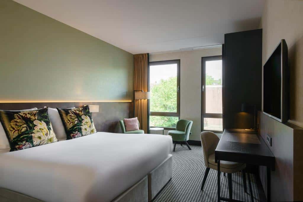 Quarto moderno do Monet Garden Hotel, que ilustra onde ficar em Amesterdão: cama grande, secretária, duas cadeiras, janelas e uma parede com pormenores em verde.