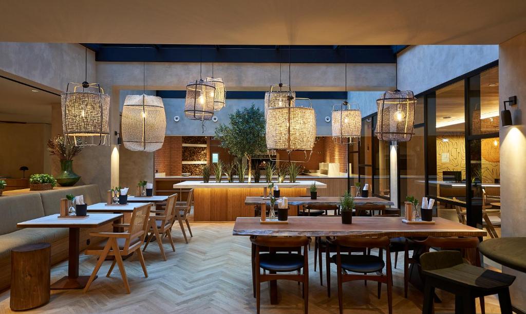 Interior de um restaurante moderno do PortoBay Teatro com mesas e cadeiras de madeira, candeeiros suspensos e plantas.