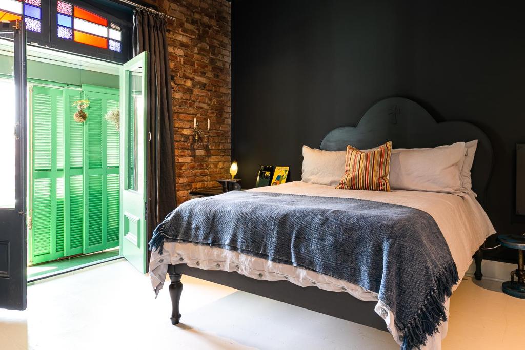 Quarto no Hotel Lola com parede escura de destaque, parede de tijolo, cama de casal, almofada colorida e portas verdes para uma varanda.