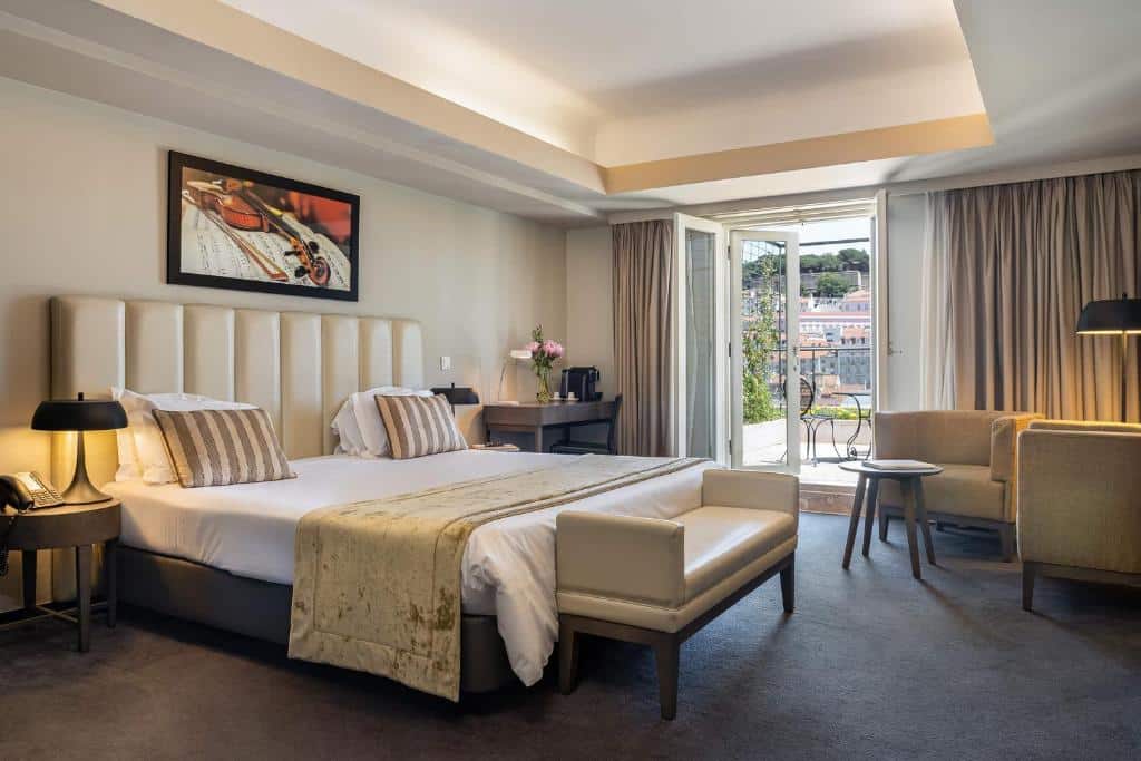 Quarto espaçoso do Hotel do Chiado com uma pequena varanda com cadeiras e uma mesinha, uma cama de casal grande, dois cadeirões, um candeeiro de pé e uma pequena mesa com comodidades para café