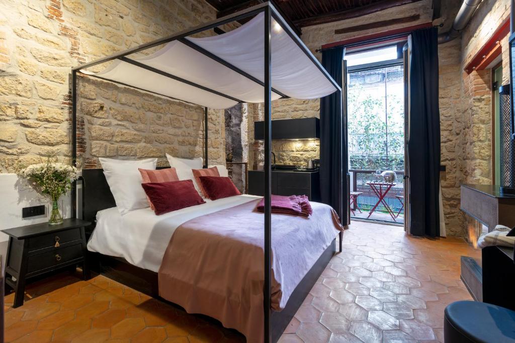 Quarto amplo do Palazzo Residenza Madre by Dimorra em estilo rústico, com paredes de pedra, cama de casal com dossel branco, almofadas vermelhas, mesa de cabeceira escura e janela com vista para o exterior.