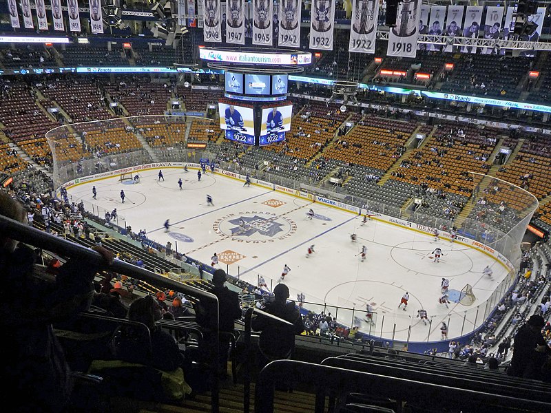 Scotiabank Arena, em Toronto, em dia de jogo de hóquei no gelo, com jogadores em campo, adeptos nas bancadas e placas retro penduradas no teto com anos marcados