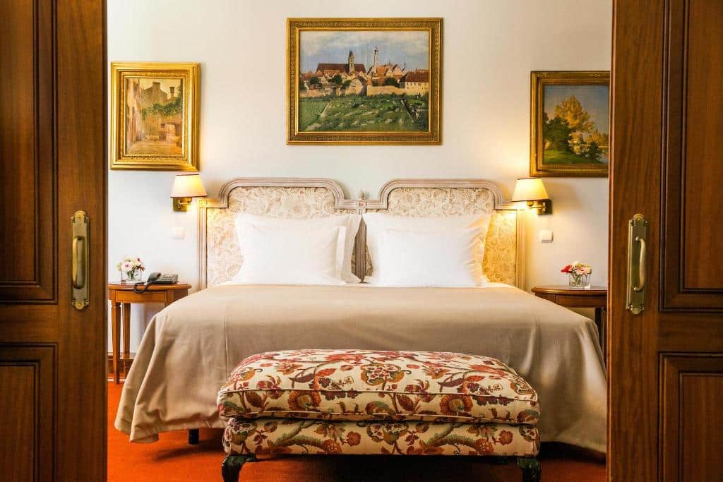 Quarto do Pestana Palace Lisboa Hotel & National Monument, com cama de casal, três quadros na parede ao fundo, um móvel estofado aos pés da cama e candeeiros de parede, num estilo de decoração de época