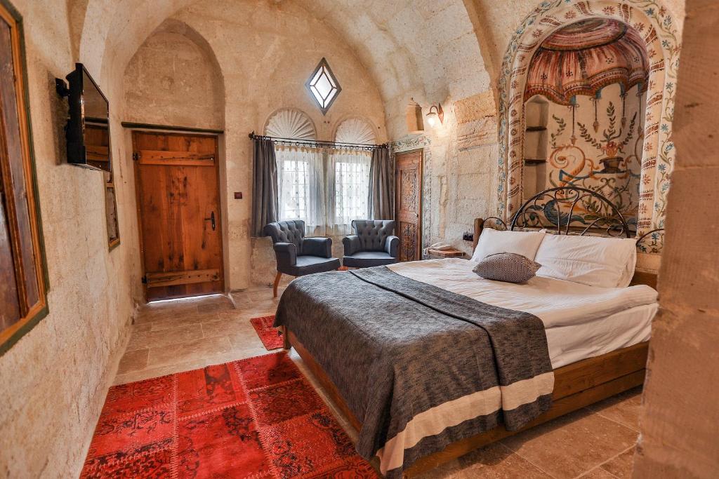 Quarto do Henna Hotel, um dos hotéis da Capadócia, com paredes de pedra e tecto em arco, cama de casal, tapete vermelho, zona de estar e duas poltronas junto à janela.