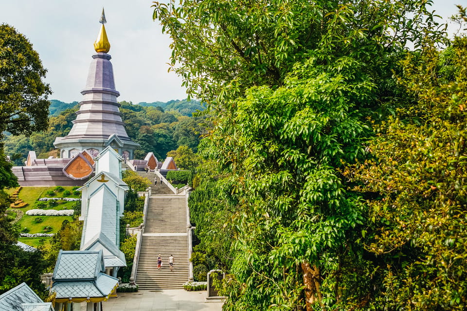 Templo com torre dourada rodeado de vegetação exuberante e uma escadaria a descer, no Parque Nacional Doi Inthanon.