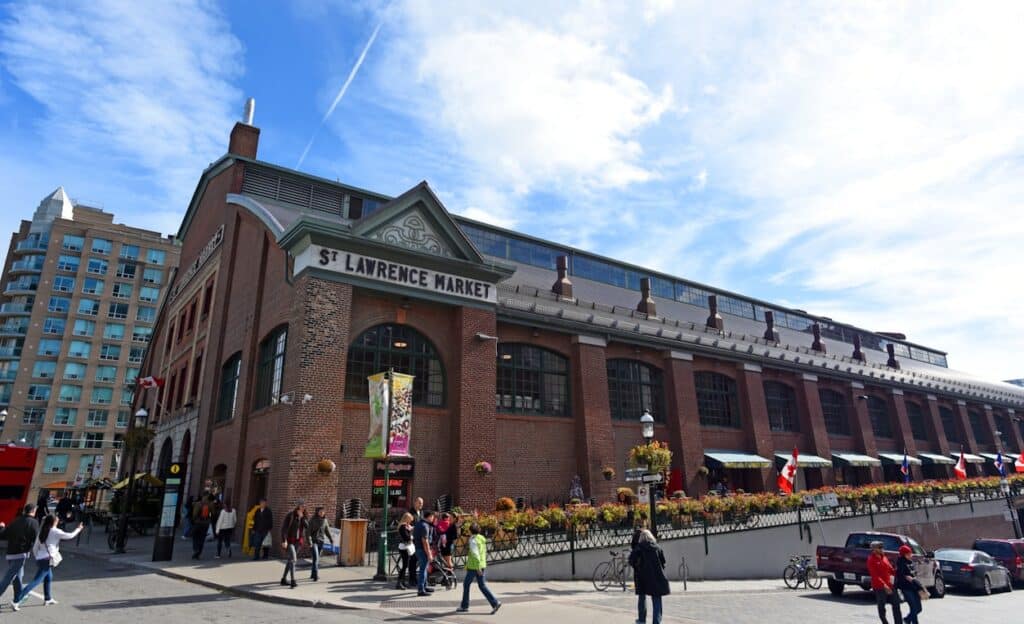 Mercado St. Lawrence, tradicional mercado público de Toronto em estilo vitoriano com pormenores arquitetónicos em tijolo vermelho e pessoas a caminhar no exterior animado