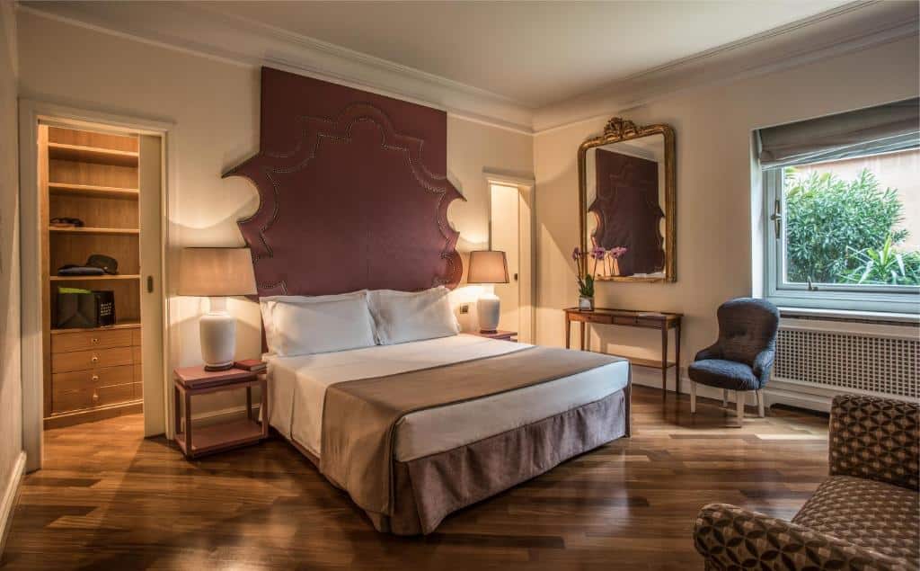 quarto do 47Luxury Suites – Colosseo, uma das opções de onde ficar em Roma, com cama de casal, mesa e candeeiro de cabeceira de cada lado, espelho grande com moldura trabalhada, mesa e cadeira