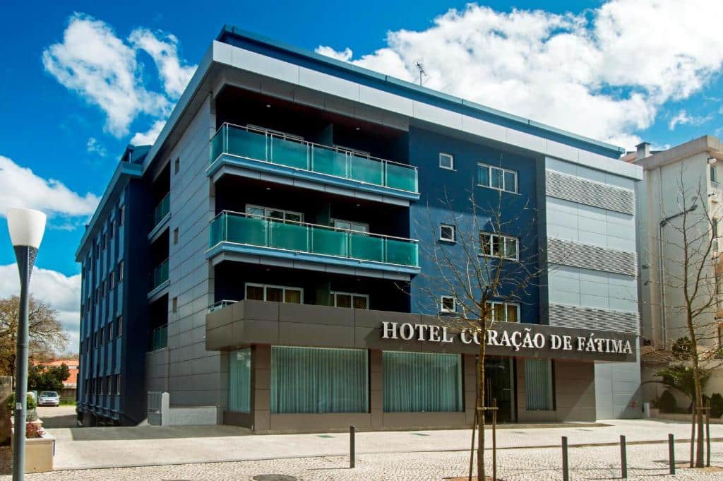 Moderno edifício de hotel de quatro andares com varandas, grandes janelas e uma placa onde se lê "Hotel Coração de Fátima".