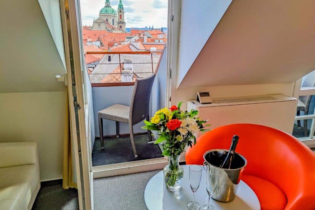 Pequena varanda do LH Vintage Design Hotel Sax, com flores, duas taças e uma garrafa de espumante, com vista para a cidade e as torres das igrejas.