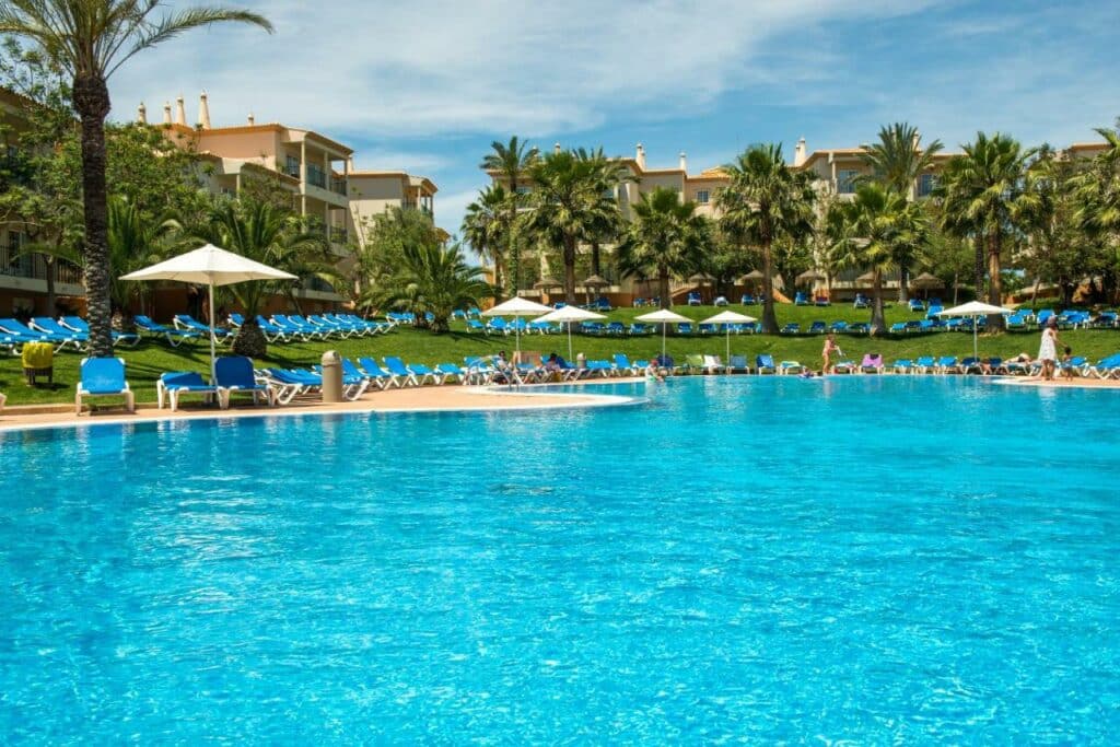 Piscina do 3HB Clube Humbria – All Inclusive a frente durante o dia e ao fundo cadeiras na borda da piscina.