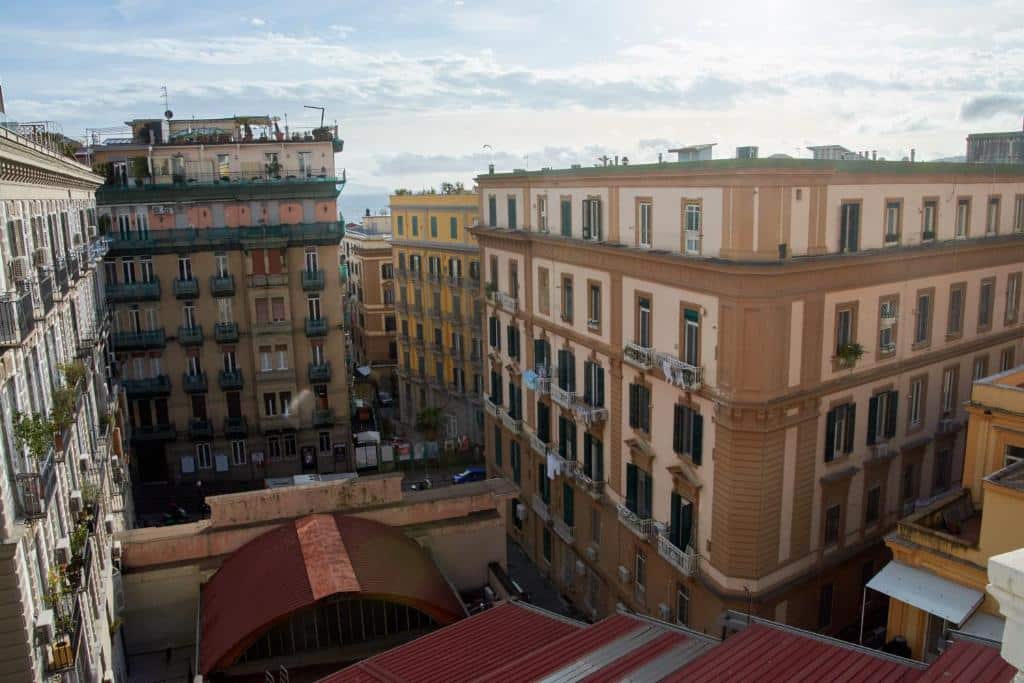 Edifícios residenciais e comerciais coloridos numa zona urbana de Nápoles, com ruas e céu nublado, junto ao Villa Margherita.