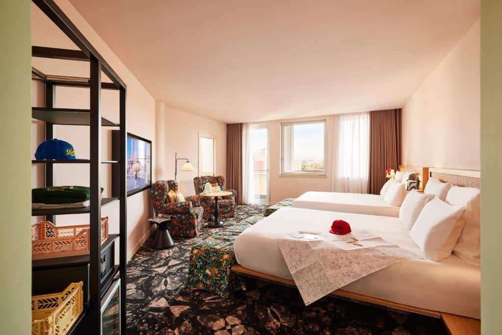 quarto do Mama Shelter Roma, um dos hotéis perto do Vaticano, com duas camas grandes, prateleiras, televisão em frente, poltronas coloridas e janelas grandes com cortinas escuras