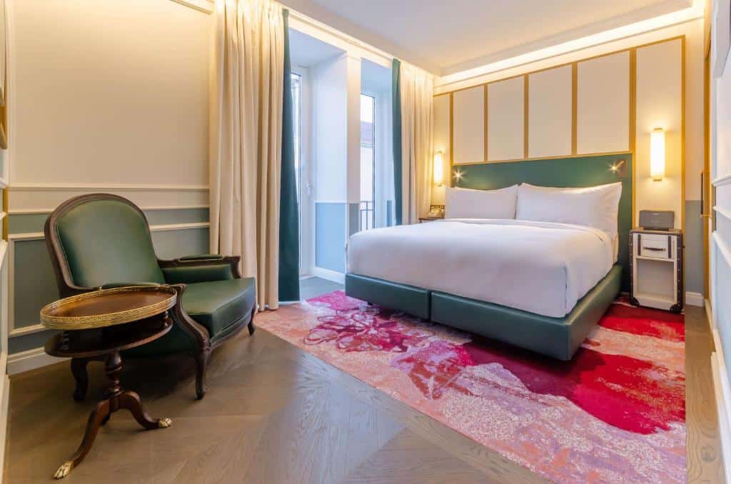 Quarto do The Emerald House Lisbon com cama de casal, varanda com cortinas, poltrona estofada e tapete