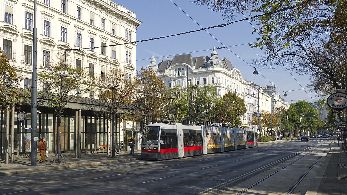 Elétrico vermelho e branco a circular numa rua da Ringstrasse, ladeada por edifícios históricos sob céu limpo.