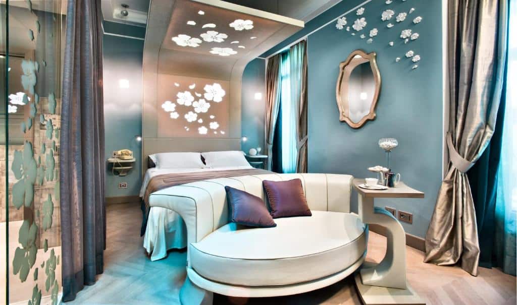 Quarto do Château Monfort – Relais &amp; Châteaux com uma cama de casal, um pequeno espelho, um sofá arredondado com almofadas, uma mesa de centro e duas janelas
