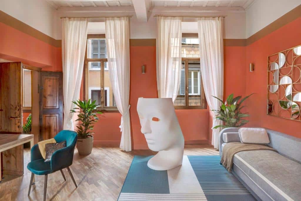 sala do Luxury Trevi House, com tapete no chão, sofá branco e duas janelas de madeira com cortinas claras, mesa e cadeira de madeira e uma escultura que representa uma máscara