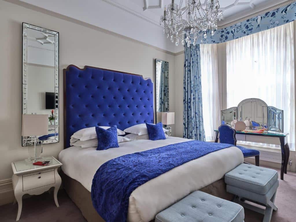 Quarto do The Apartments by The Sloane Club com cama de casal, dois espelhos, um lustre, uma janela com cortinas, um toucador, dois aparadores e duas mesas de cabeceira.