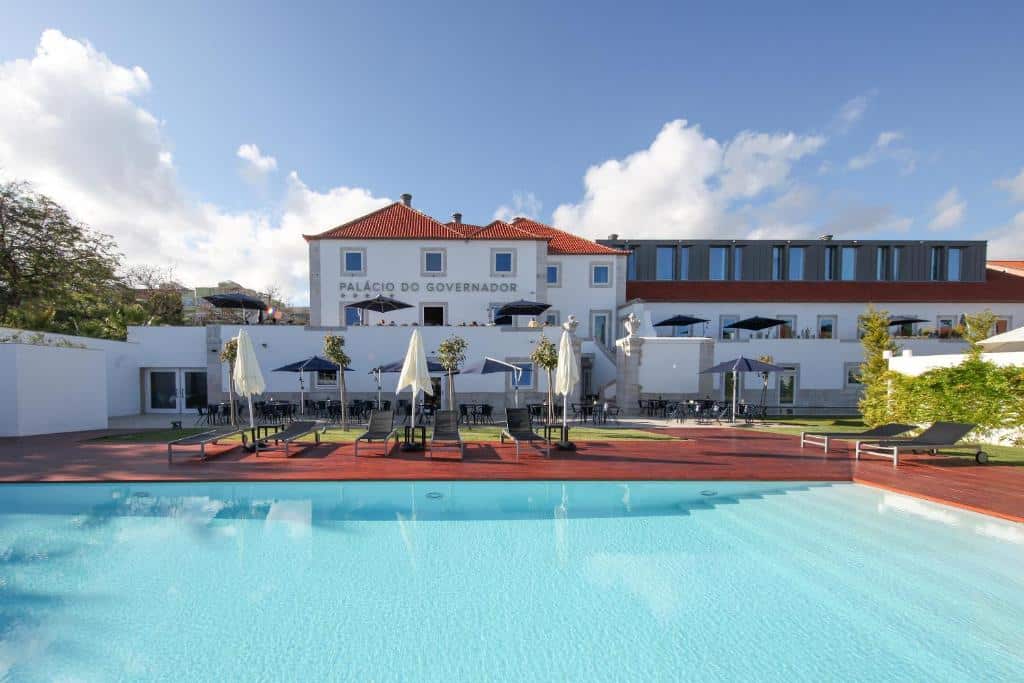 Piscina ampla do NAU Palacio do Governador rodeada por um deck de madeira com espreguiçadeiras e chapéus de sol brancos