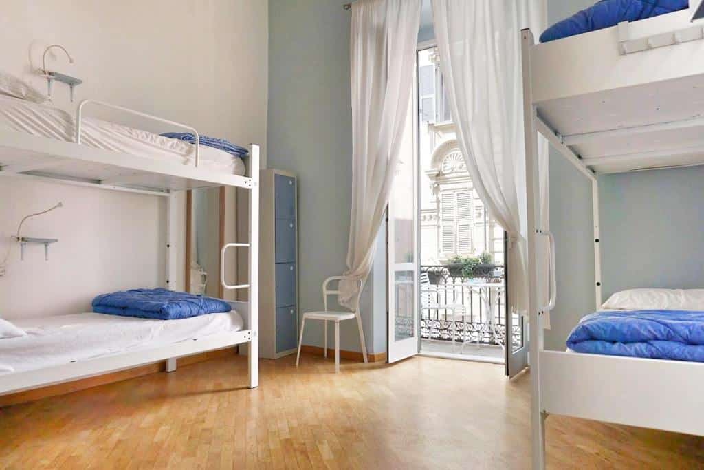 Quarto com quatro beliches brancos no Grand Hostel Manin, com porta de vidro para a varanda