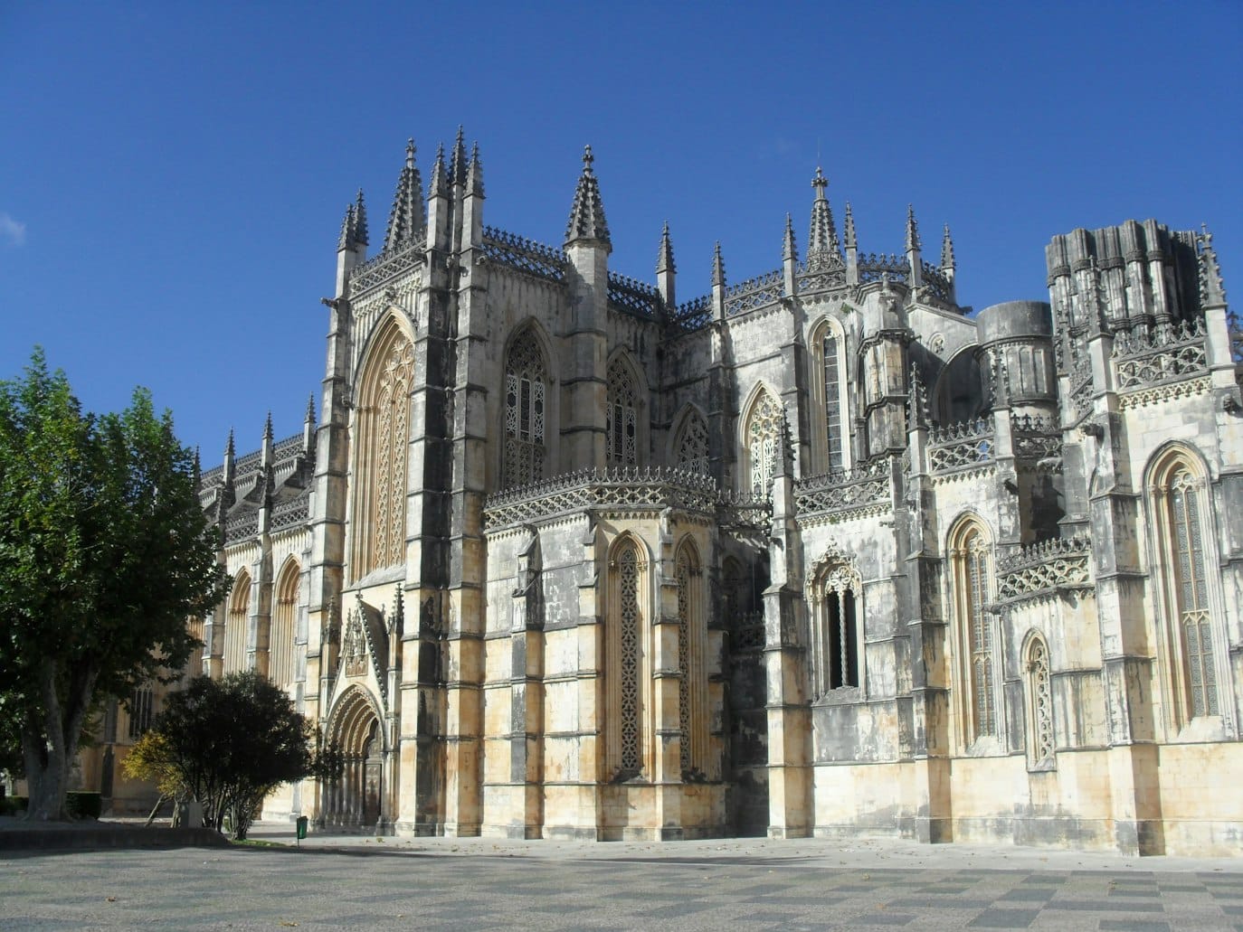 Mosteiro da Batalha, em pedra de estilo gótico, com torres ornamentadas e janelas em arco, contra um céu azul claro.