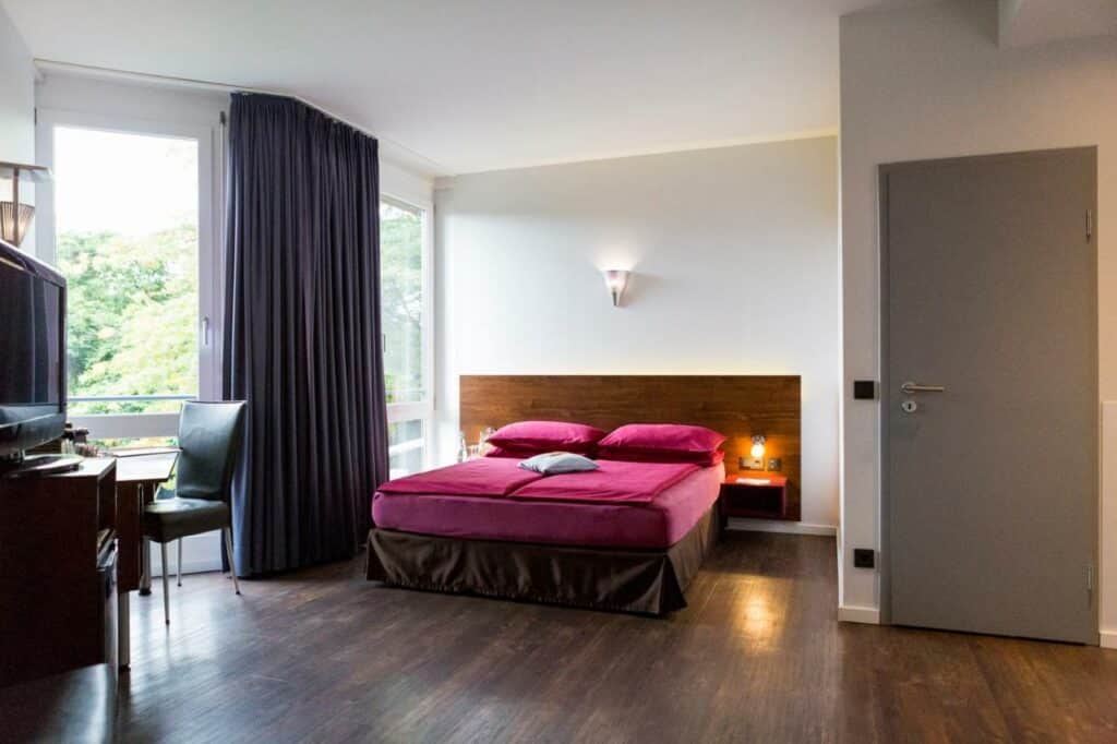 Quarto do Auszeit Hotel Düsseldorf com cama de casal ao centro e secretária de trabalho. Representa hotéis em Dusseldorf.