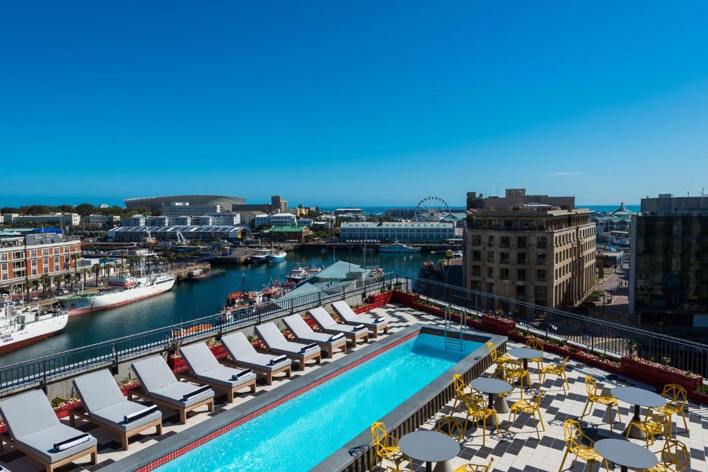 Piscina na cobertura do Radisson RED Hotel com espreguiçadeiras e vista para o porto, os edifícios e uma roda-gigante.
