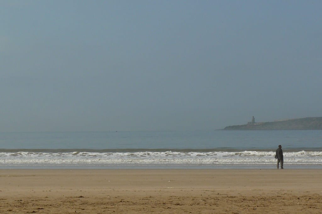 Um homem sozinho, no canto direito, à beira-mar na praia de Essaouira.