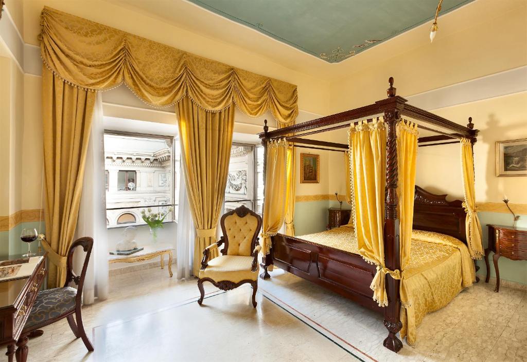 Quarto de estilo clássico do Hotel Art Resort Galleria Umberto com cama de dossel em madeira entalhada, cadeira estofada e cortinas douradas com pormenores ornamentados.