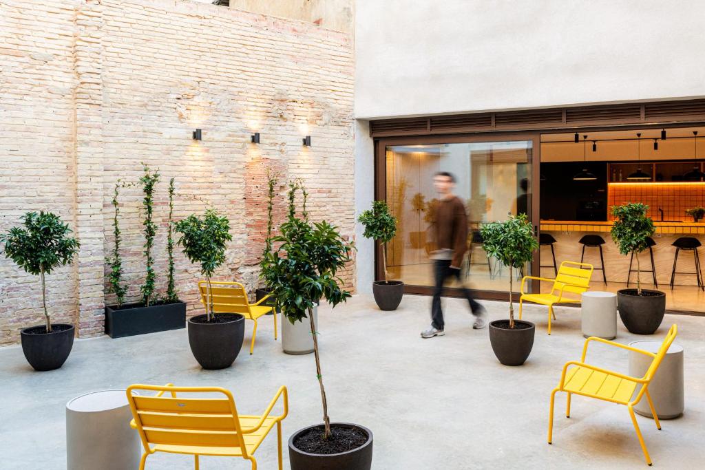 Pátio interior de um espaço moderno do Colo Colo Hostel Valencia, com paredes de tijolo, plantas em vasos e móveis de design com apontamentos amarelos.