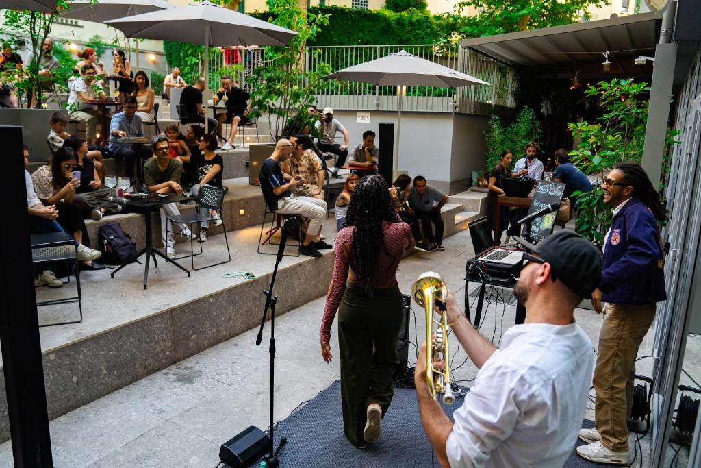 Espaço partilhado do 21 House of Stories Città Studi com jardim, mesas e cadeiras e uma banda a atuar no local