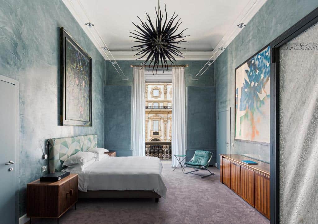 Quarto moderno e artístico do Galleria Vik Milano com uma varanda com vista para uma galeria, uma cama de casal, teto alto com um lustre que imita uma bola com tentáculos pretos, uma poltrona e um móvel de madeira