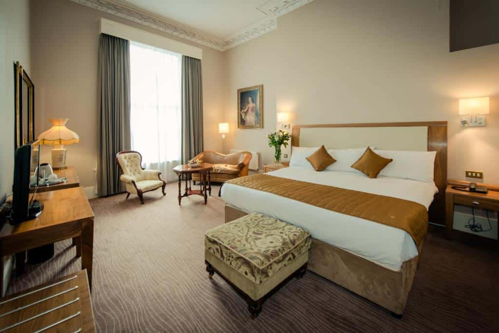 Quarto do Albany House com cama de casal, poltrona e mobiliário de madeira, decorado em tons neutros.
