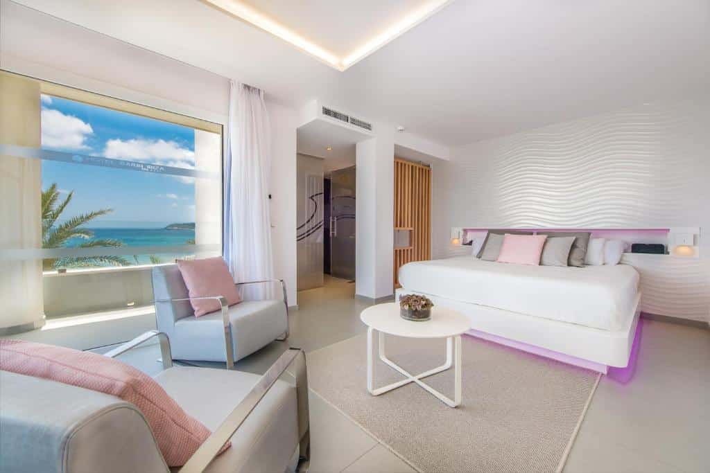 Quarto moderno do Hotel Garbi Ibiza & Spa com cama de casal, zona de estar e vista para o mar através de uma grande janela.
