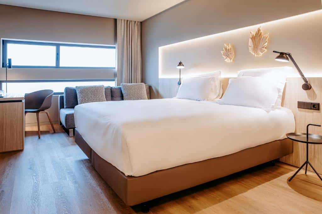 Quarto moderno do Mercure Fátima com uma cama de casal, sofá, secretária, janela, candeeiros de parede e decoração em tons neutros, para representar onde ficar em Fátima.