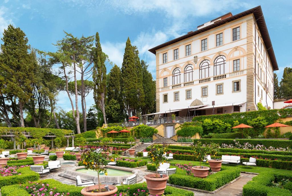 Jardim amplo à entrada do Il Salviatino, um dos hotéis na Toscana, com flores coloridas, vasos de barro, relvado verde e o edifício clássico da propriedade