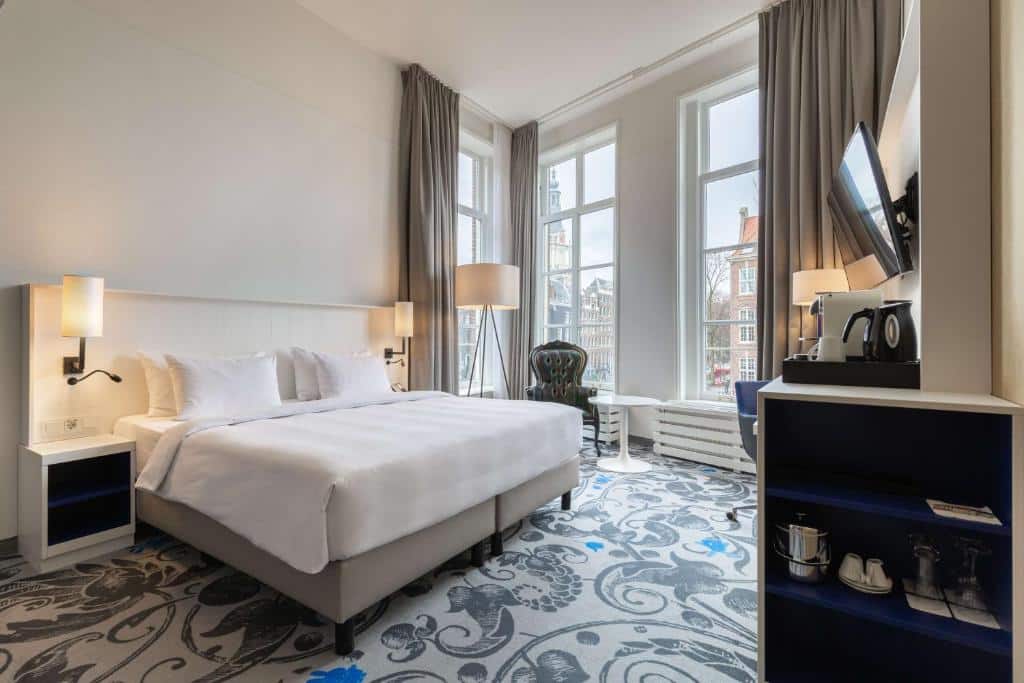 Quarto moderno do Radisson Blu Hotel, que ilustra onde ficar em Amesterdão: cama grande, secretária, TV, zona de café, poltrona e janelas grandes com vista para a cidade.