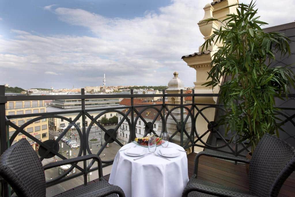 Pequena mesa redonda com duas cadeiras numa varanda do Hotel Kings Court, com vista sobre os edifícios da cidade sob um céu parcialmente nublado.