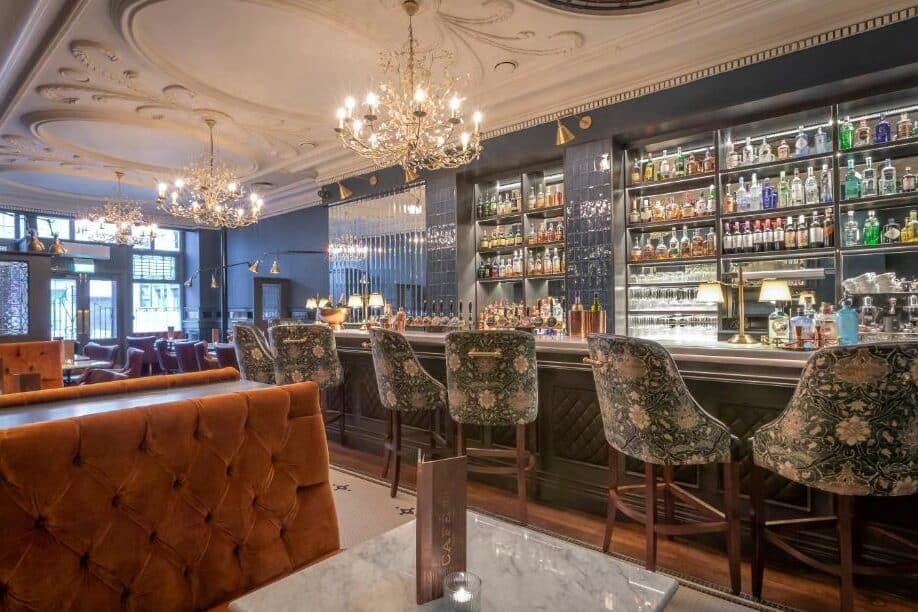 Bar sofisticado no The Fleet, em estilo clássico, decorado com candelabros de cristal, paredes escuras e requintado mobiliário estofado.