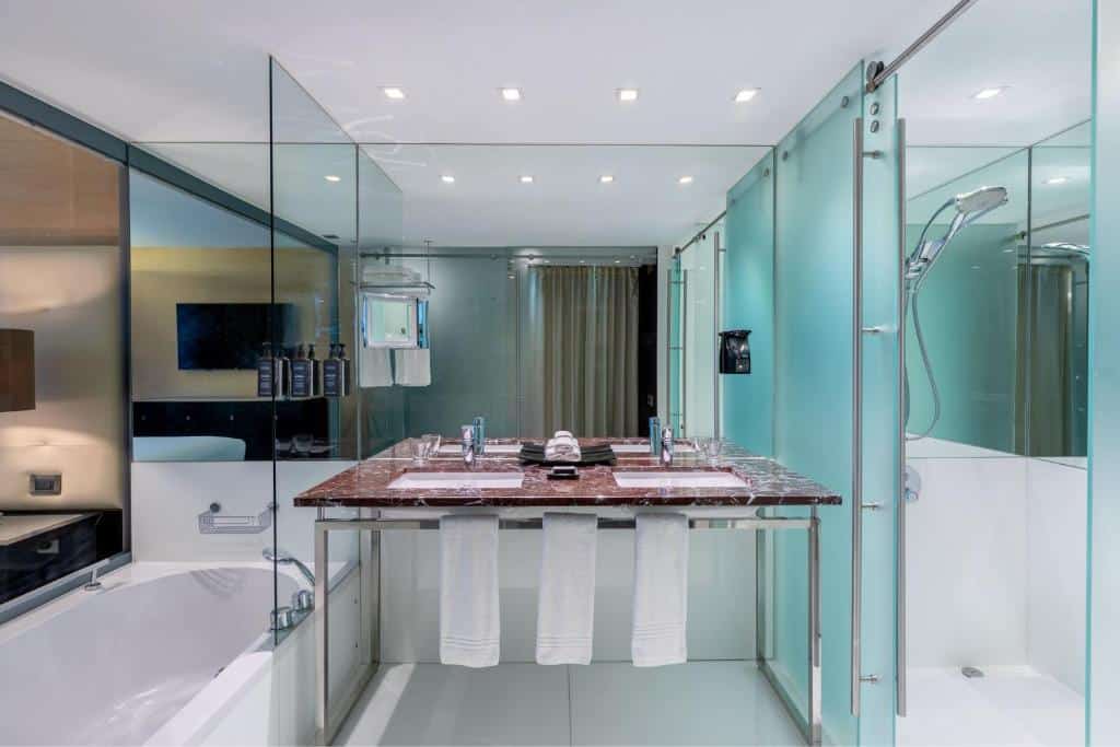 Casa de banho moderna do Sheraton Lisboa Hotel & Spa com chuveiro com resguardo de vidro, lavatório duplo com bancada castanha e banheira branca com acessórios elegantes.