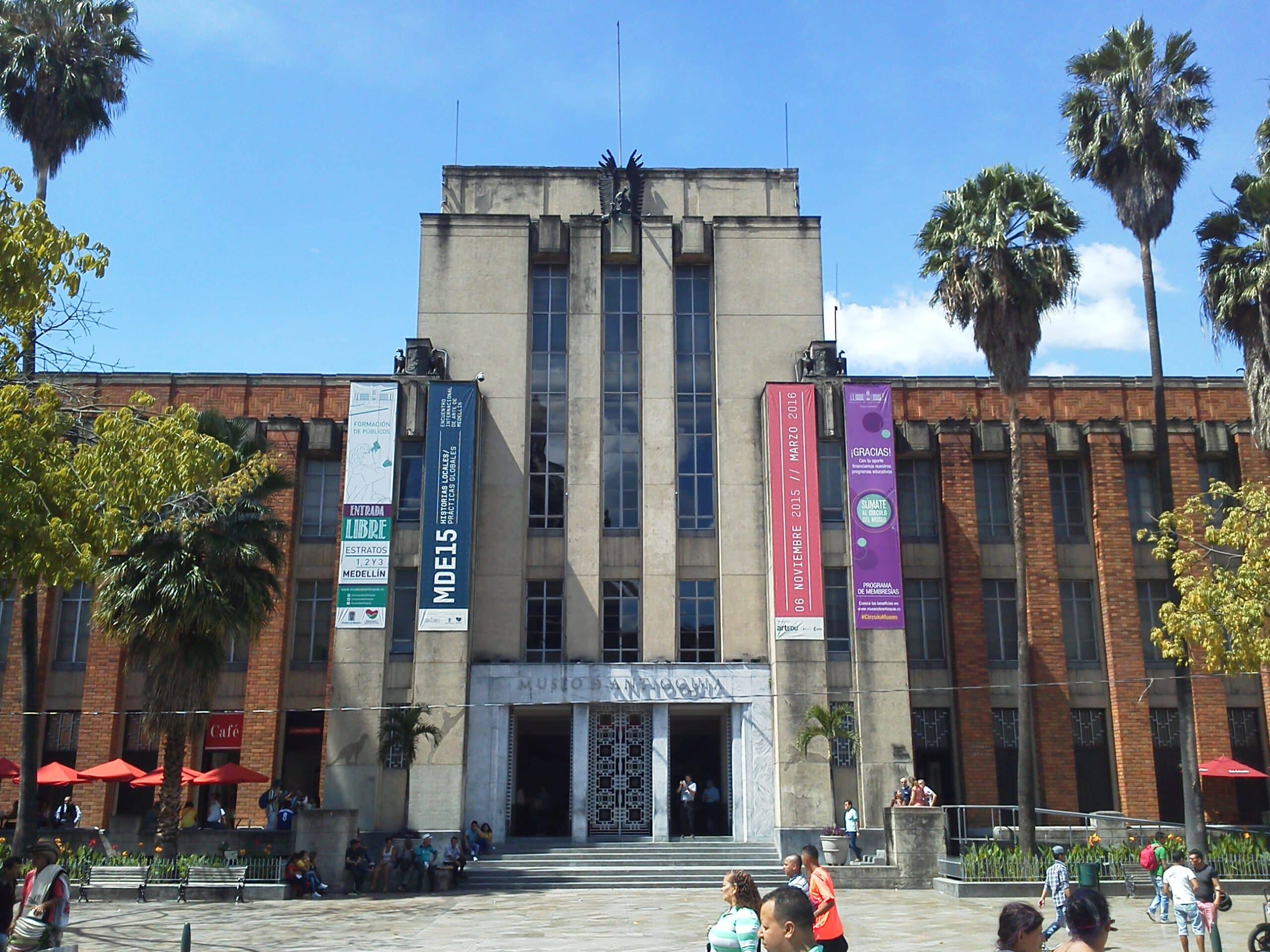 Fachada do Museo de Antioquia, com três faixas verticais e palmeiras à frente.