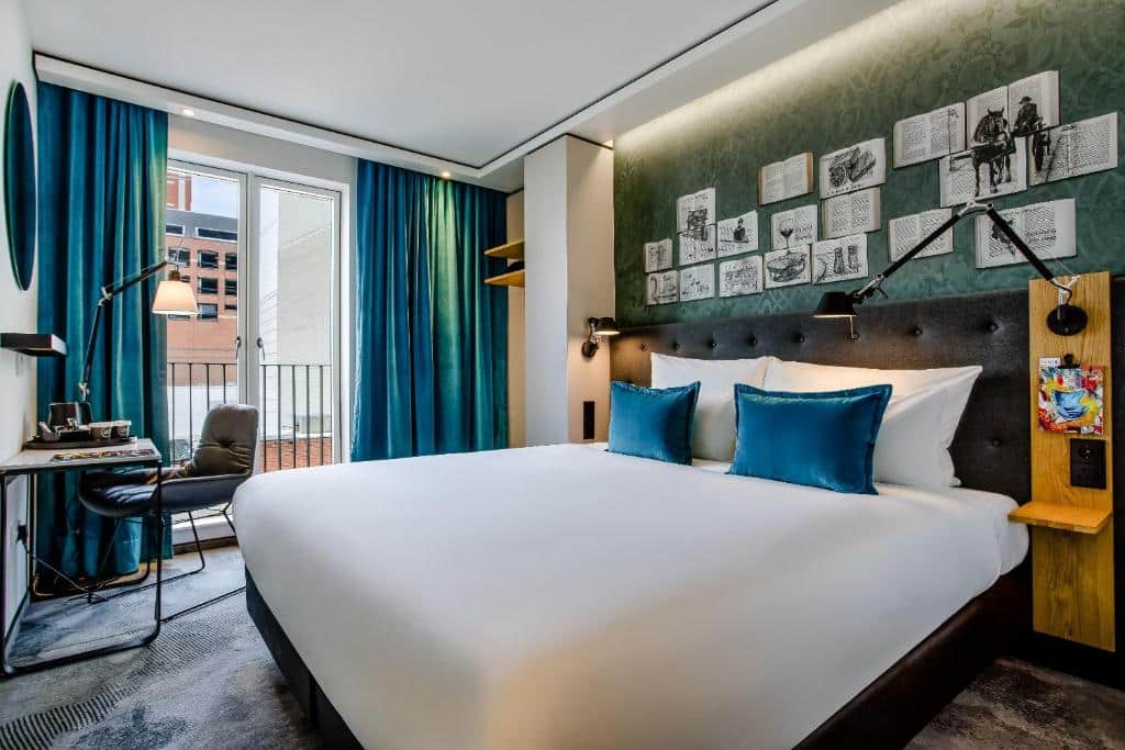 Quarto do Motel One Dublin com paredes verdes, cortinas azuis e decoração em preto e madeira.