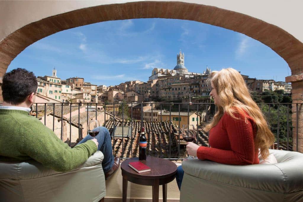 Casal a provar vinho numa varanda com vista para a cidade histórica de San Gimignano, Itália