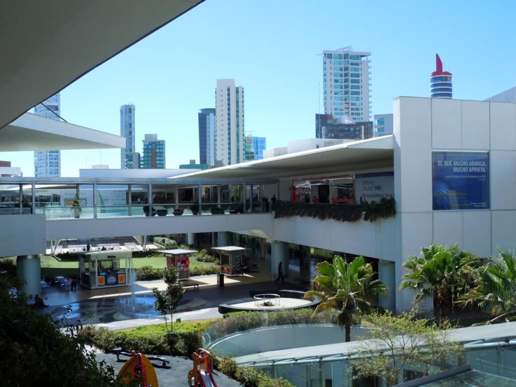 Centro Comercial Andares, espaço comercial moderno com edifícios de escritórios e torres residenciais ao fundo, em cenário urbano com céu azul e vegetação.