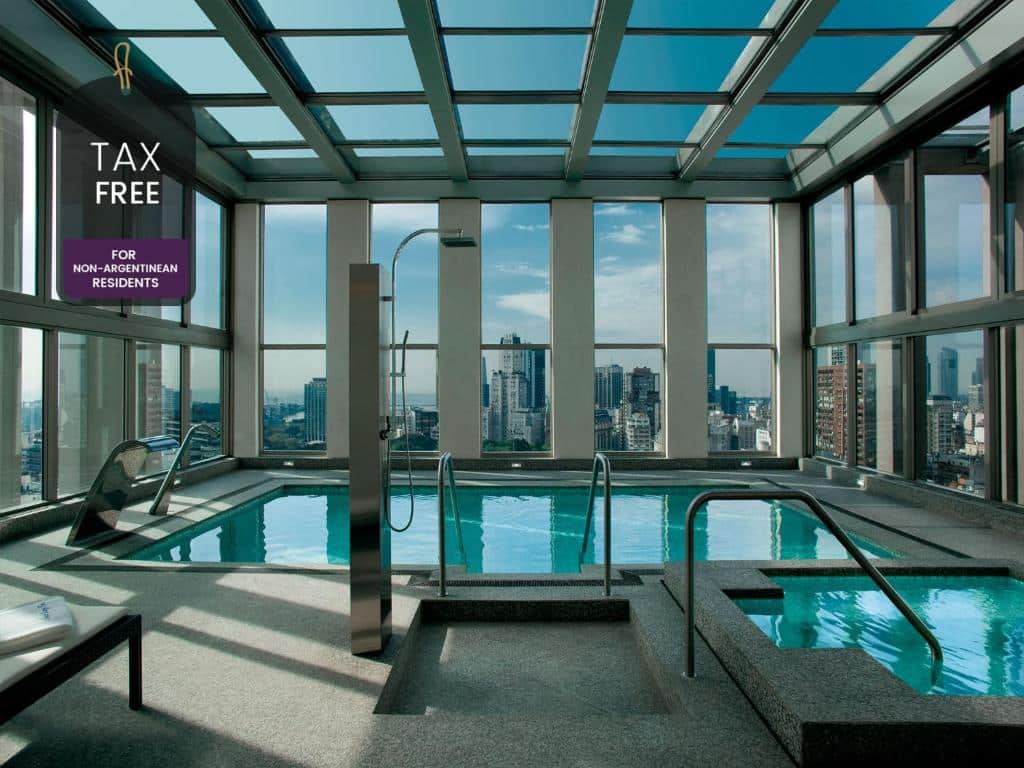 piscina coberta do Alvear Art Hotel, num andar alto com paredes de vidro e vista panorâmica de Buenos Aires, com espreguiçadeiras junto às janelas