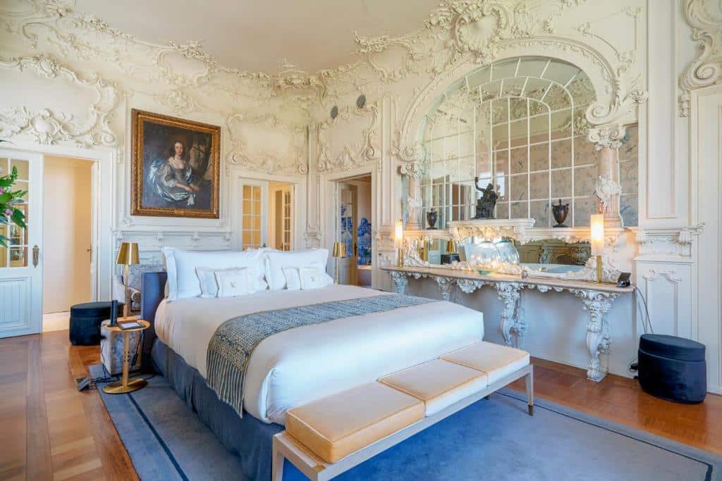 Quarto luxuoso do Verride Palácio Santa Catarina, com cama de casal grande, paredes trabalhadas em estuque, quadros e espelhos num estilo renascentista, e um tapete por baixo da cama
