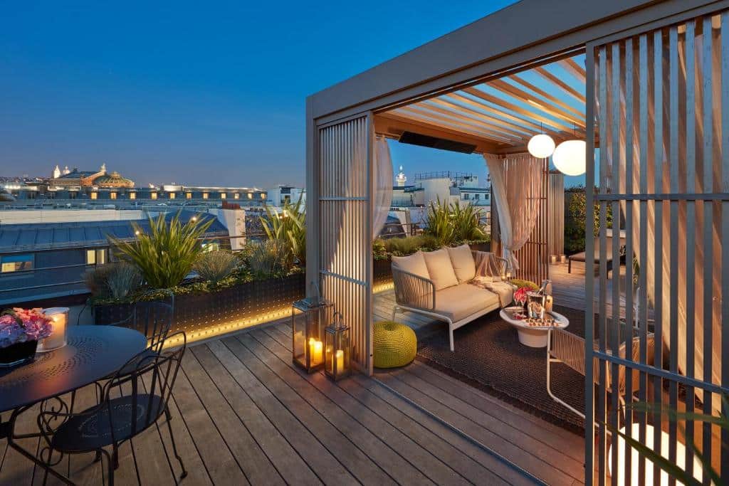 Um terraço na cobertura do Mandarin Oriental, Paris ao anoitecer com assentos sob uma pérgola, lanternas, vasos de plantas e uma vista da cidade ao fundo. Este é um dos hotéis de luxo em Paris.