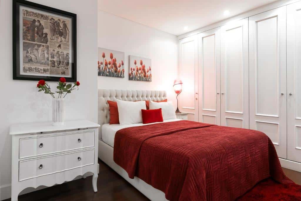 Quarto do Lisbon Rentals Chiado em vermelho e branco, com roupeiros, uma cama de casal com cabeceira estofada e uma cómoda de época com duas gavetas e um vaso com rosas