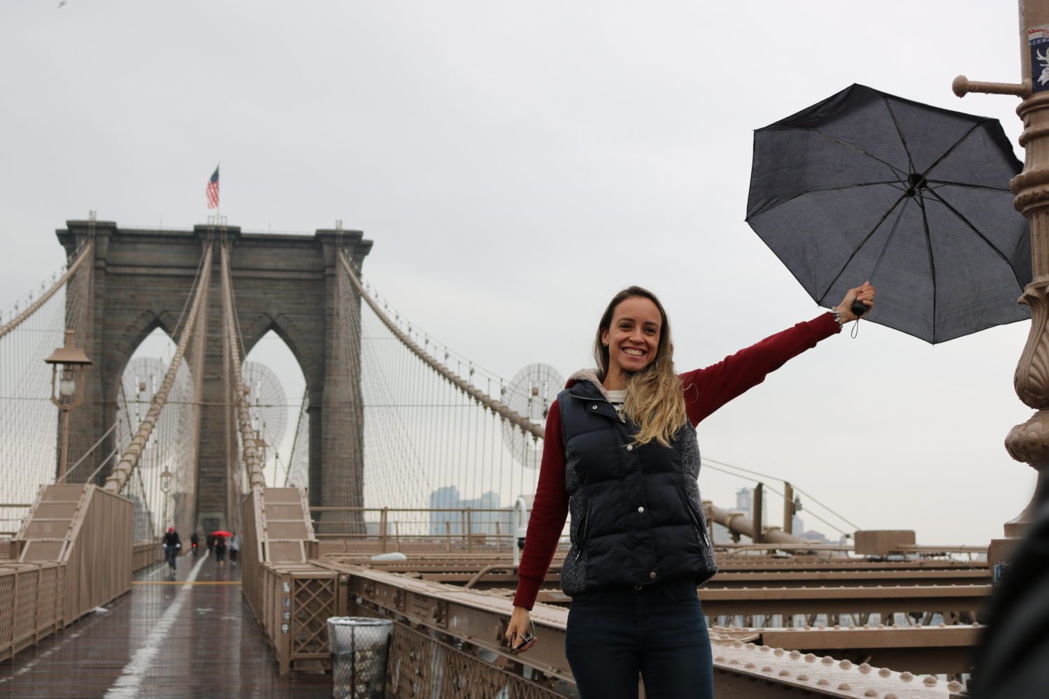 Passadiço para peões da Ponte do Brooklyn, com uma torre e a bandeira norte-americana ao fundo.